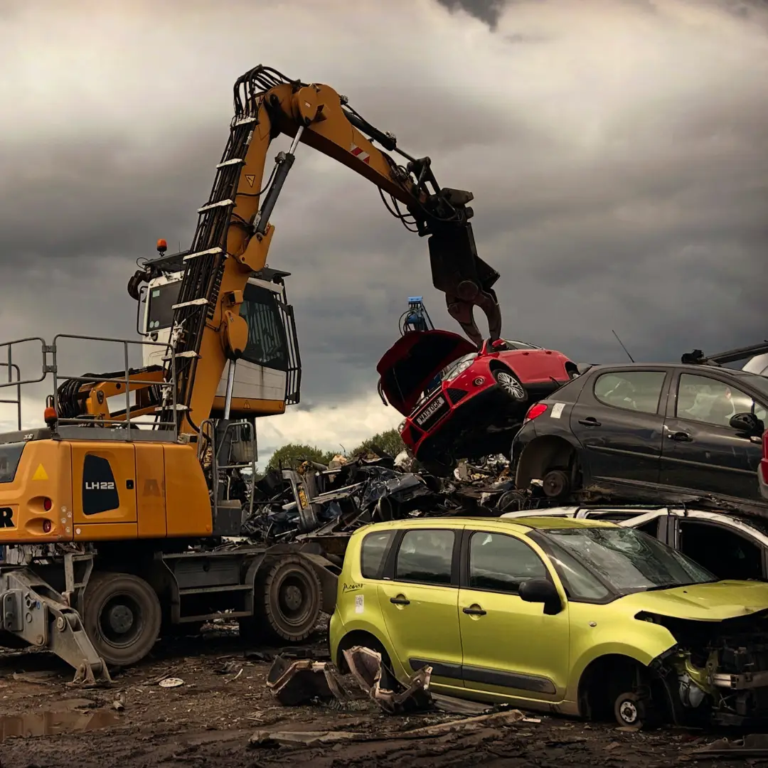 Excavator lifting red car in scrapyard