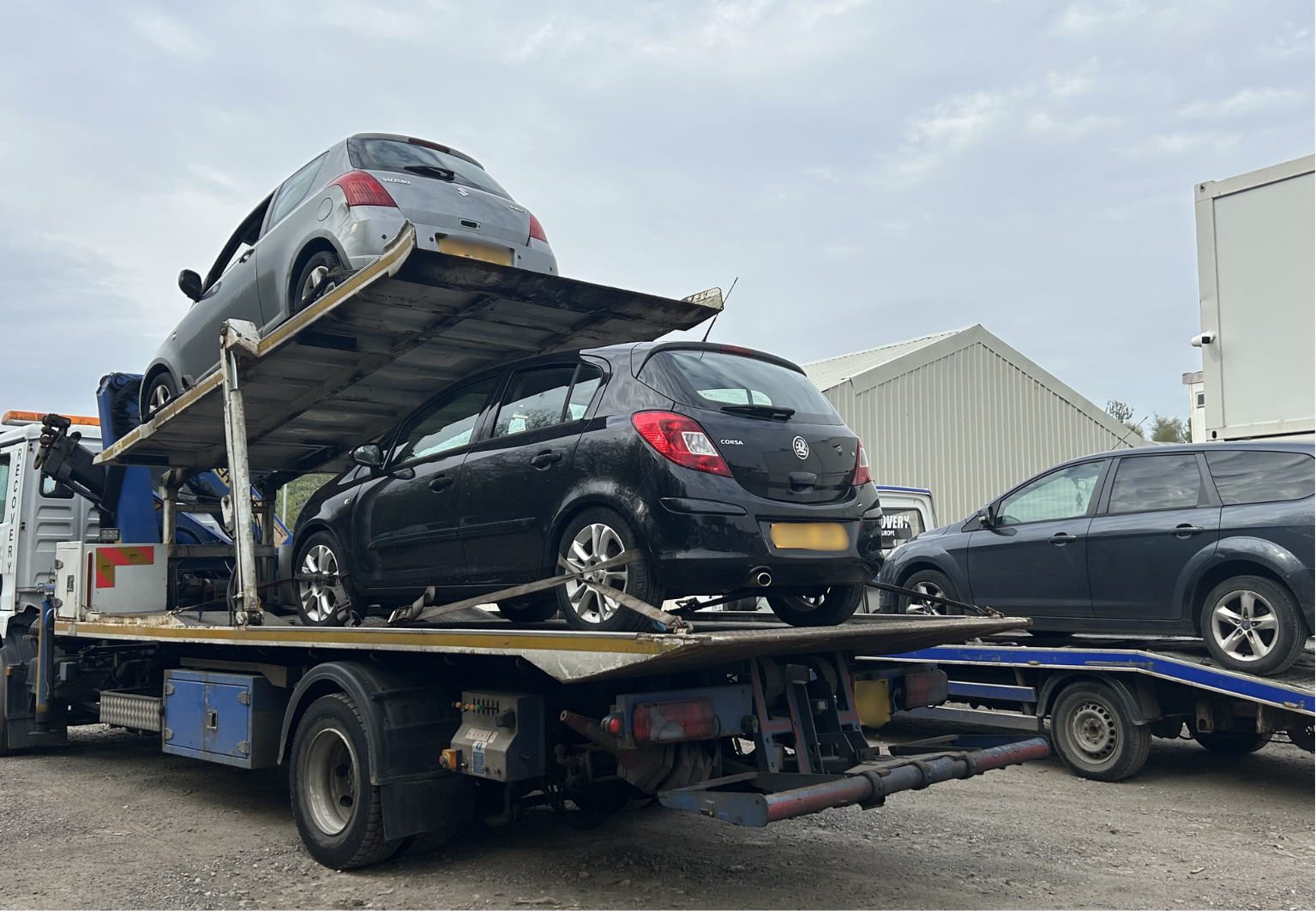 Car transporter carrying two hatchbacks in yard