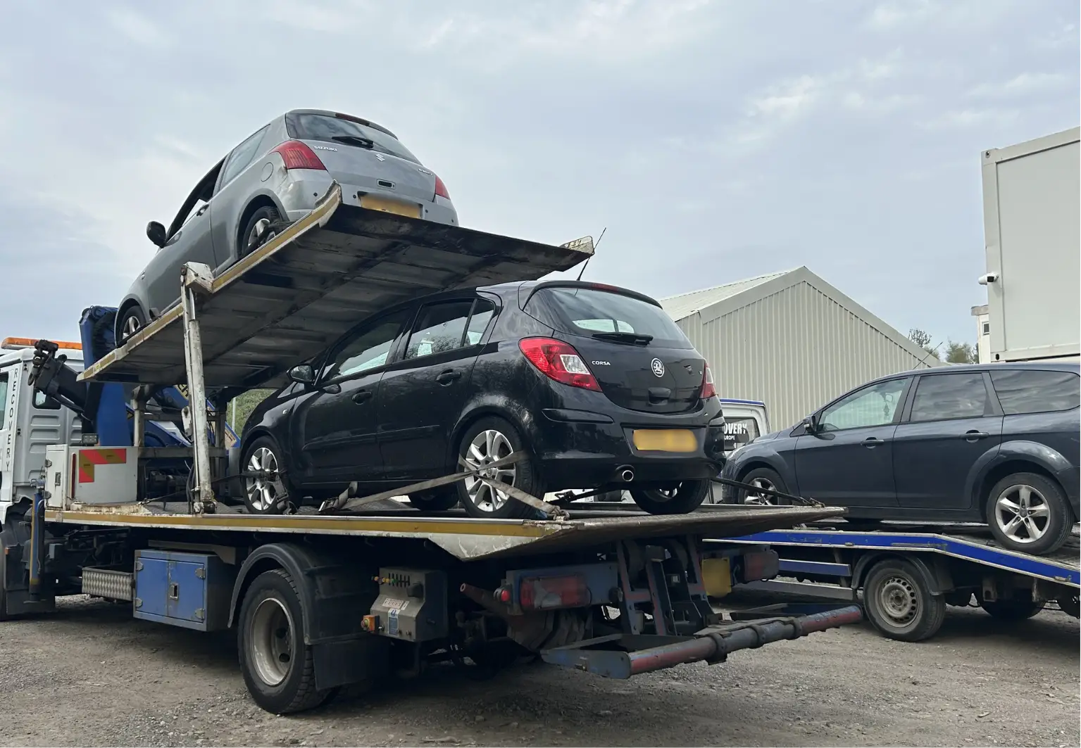 Car transporter carrying two hatchbacks in yard