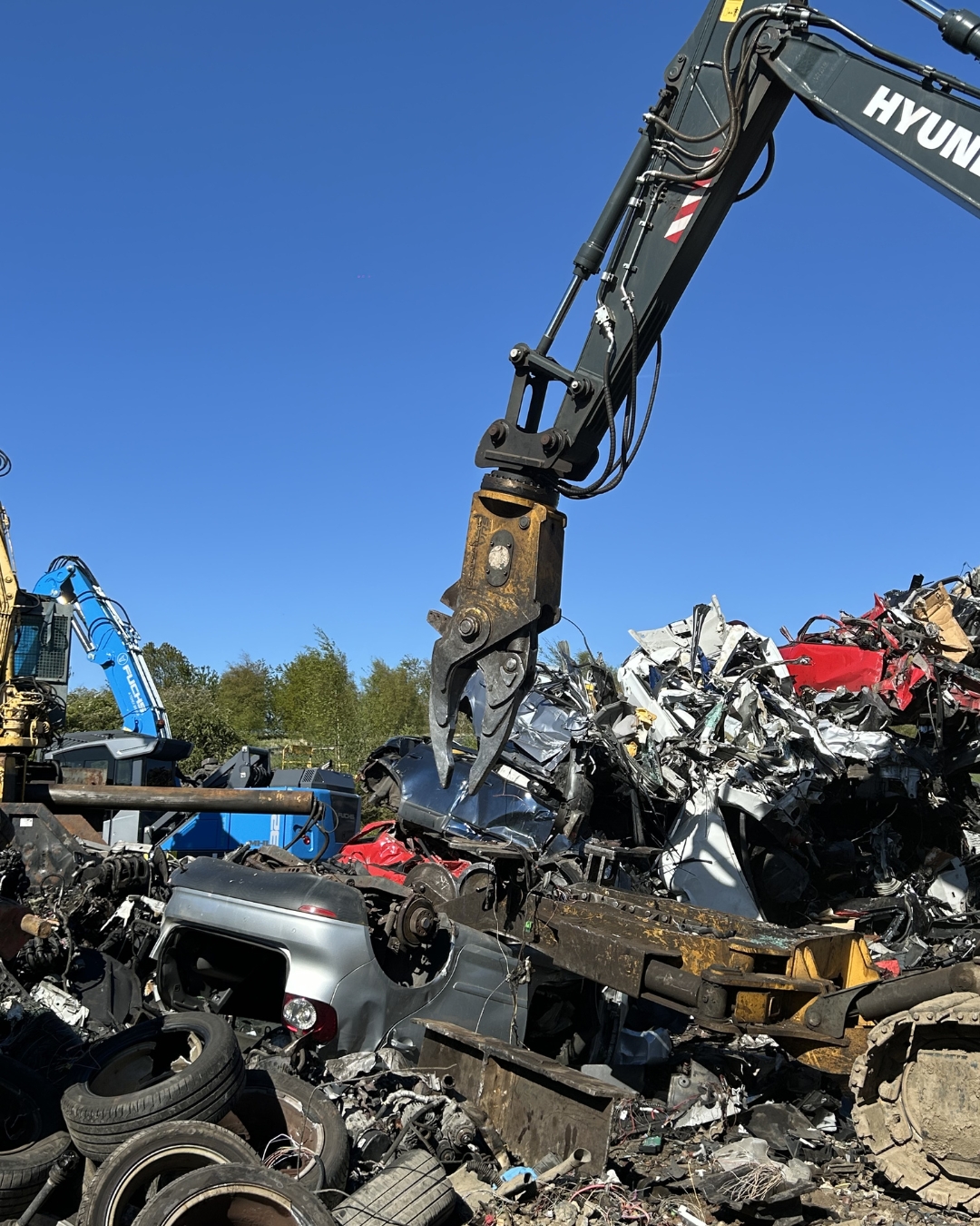 Excavator claw crushing scrap cars in scrapyard