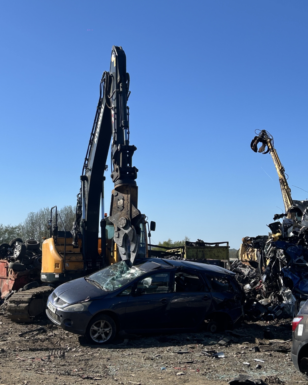 Excavators crushing cars in scrapyard under blue sky