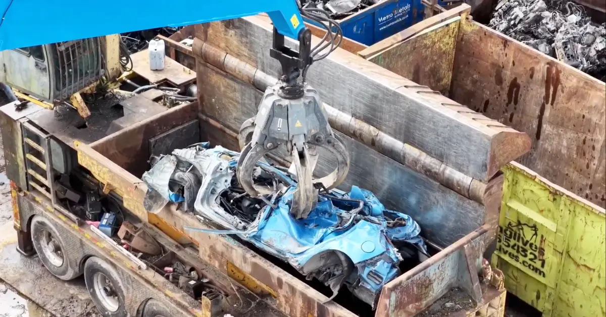 Crane lifting crushed blue car into scrap container