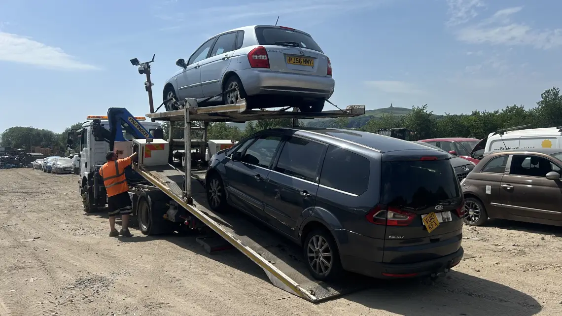 Car transporter loading vehicles at scrapyard